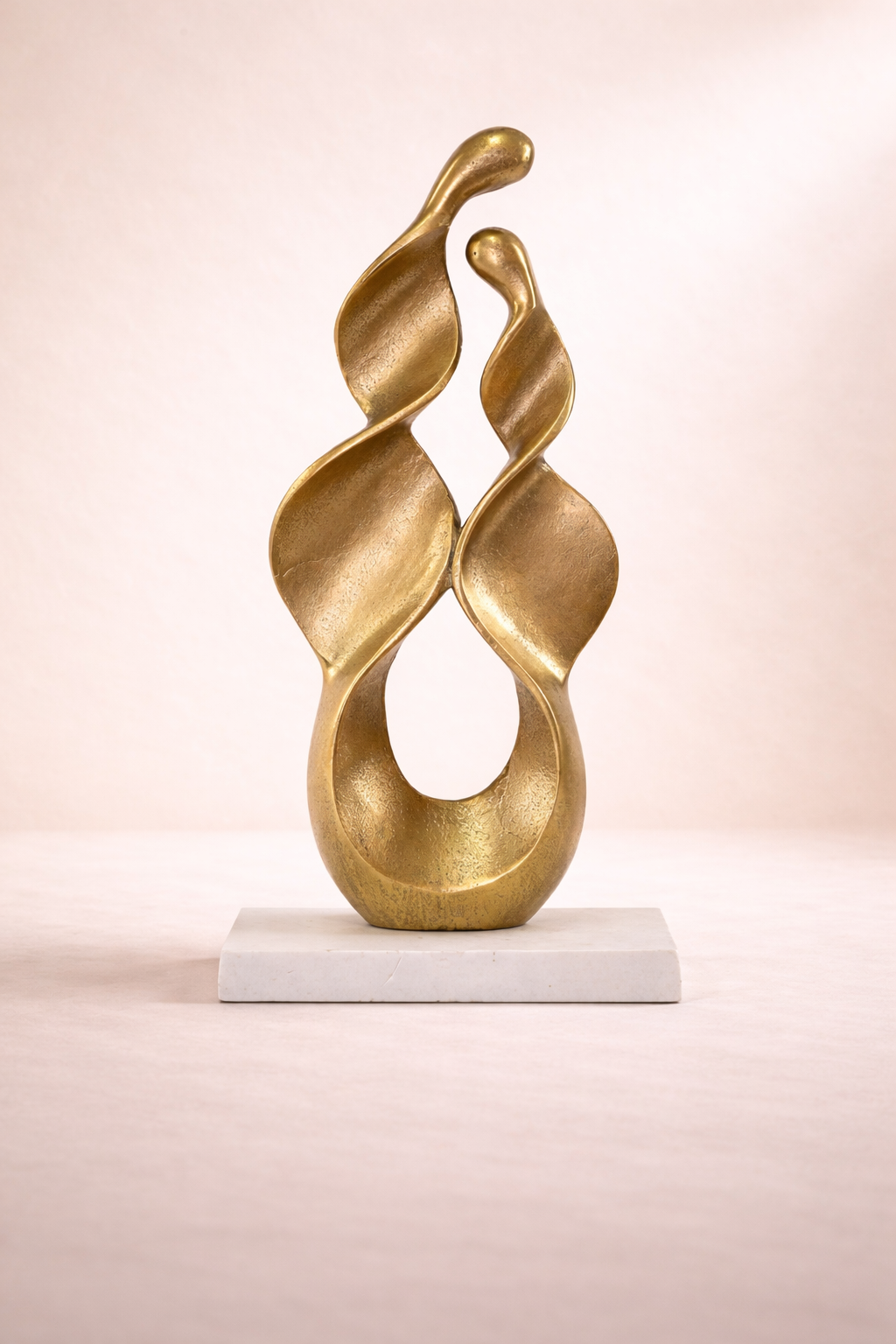 Gold abstract sculpture on a white base against a light pink background
