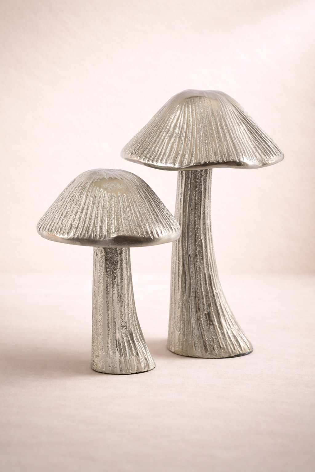 Two silver mushroom-shaped decorative items on a light pink background
