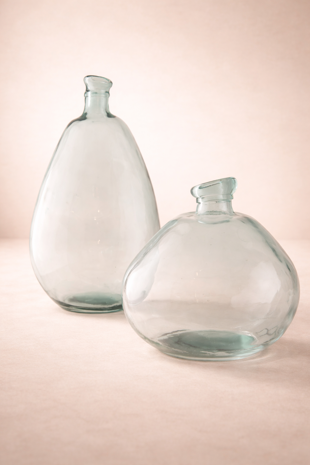 Two clear glass bottles on a light pink background