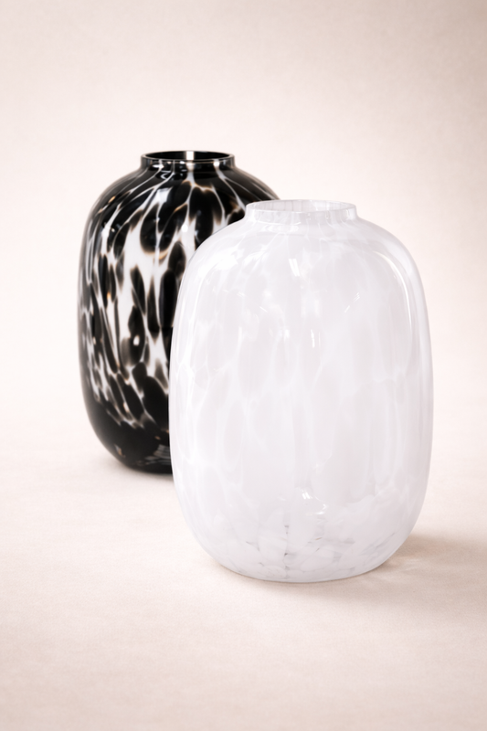 Two glass vases, one black and white patterned and the other plain white, on a light beige background.