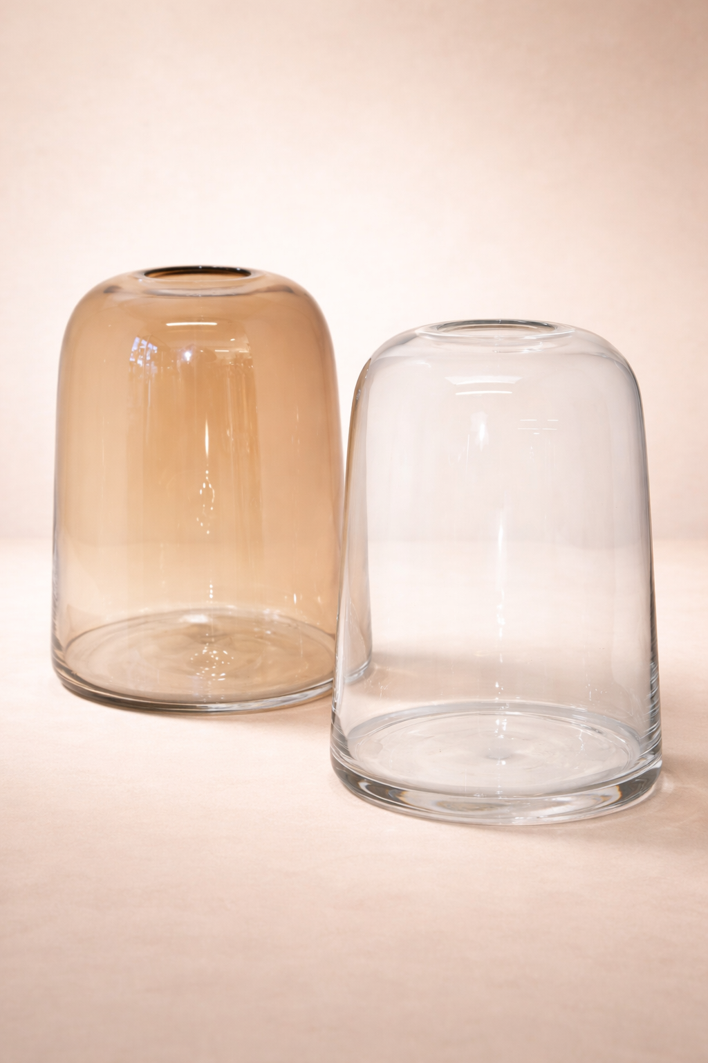 Two glass vases, one brown and one clear, on a beige background