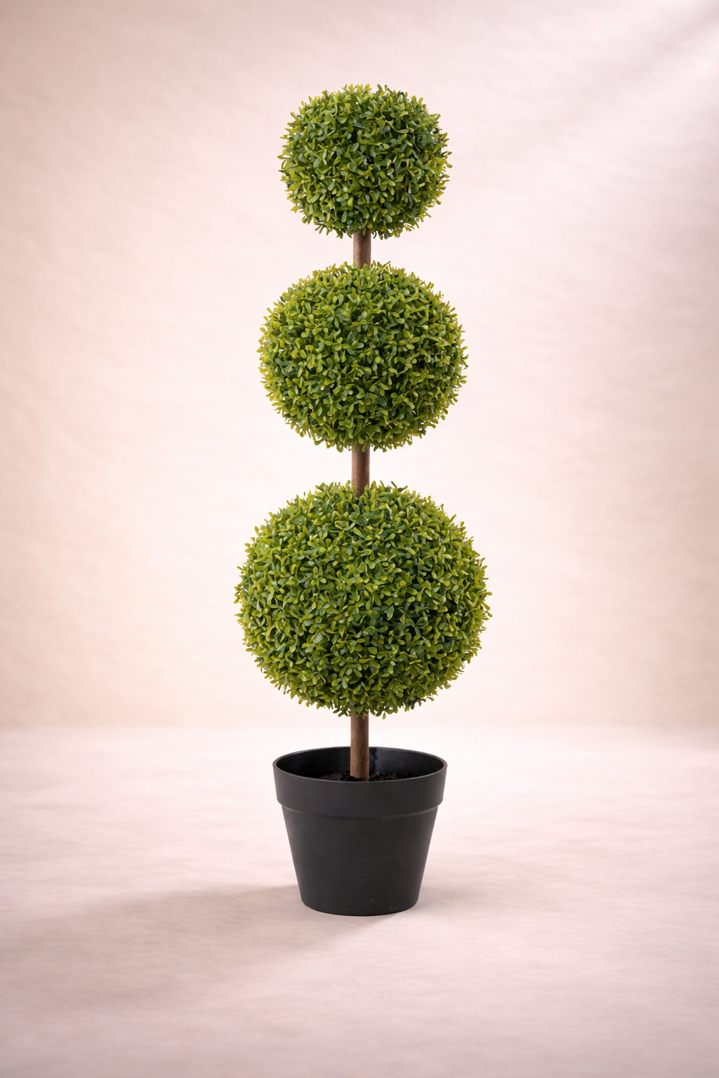 Three-tiered artificial topiary plant in a black pot on a beige background