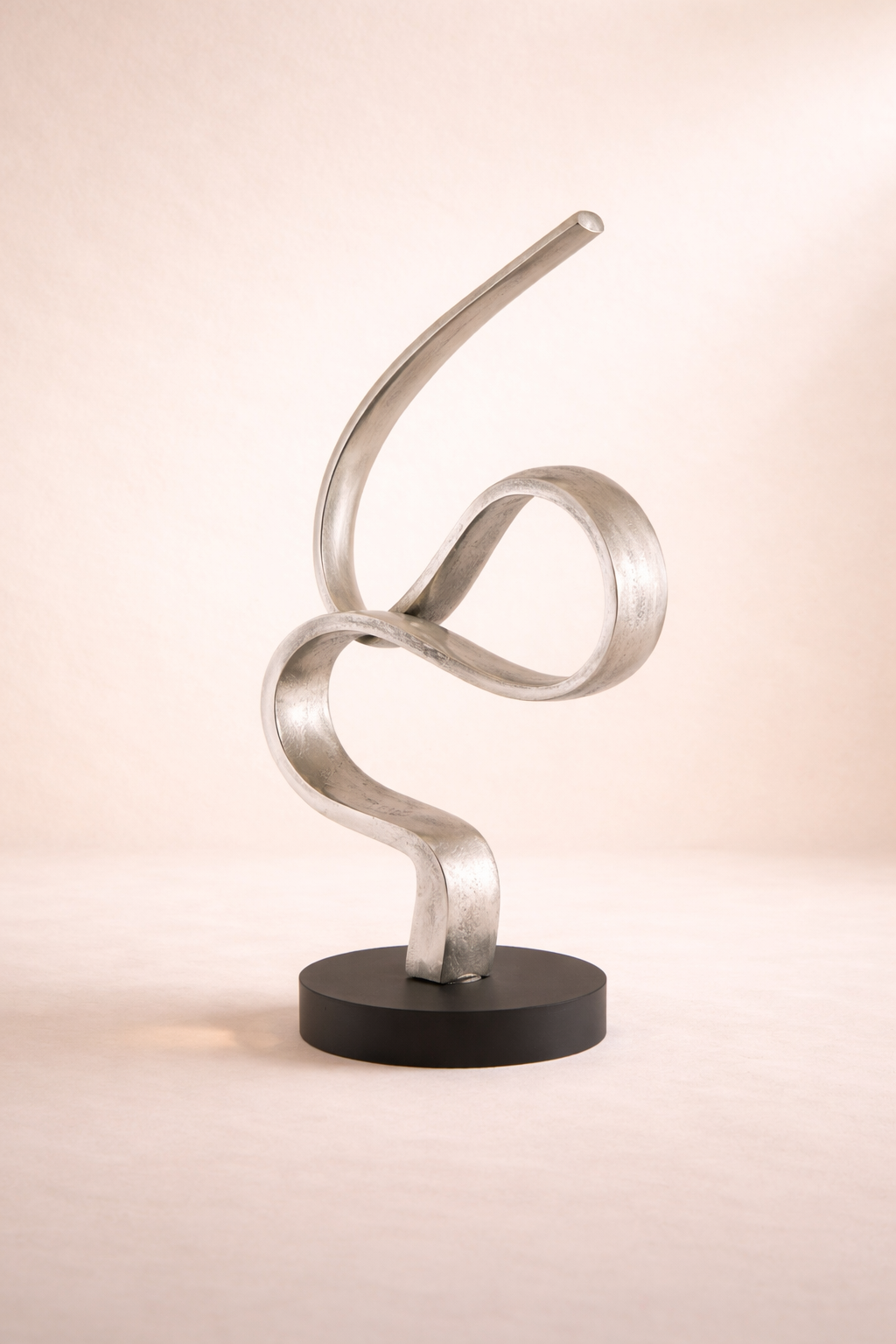 Modern metal sculpture on a black base against a beige background