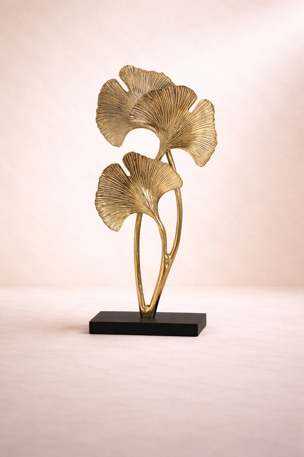 Gold leaf sculpture on a black base against a pink background