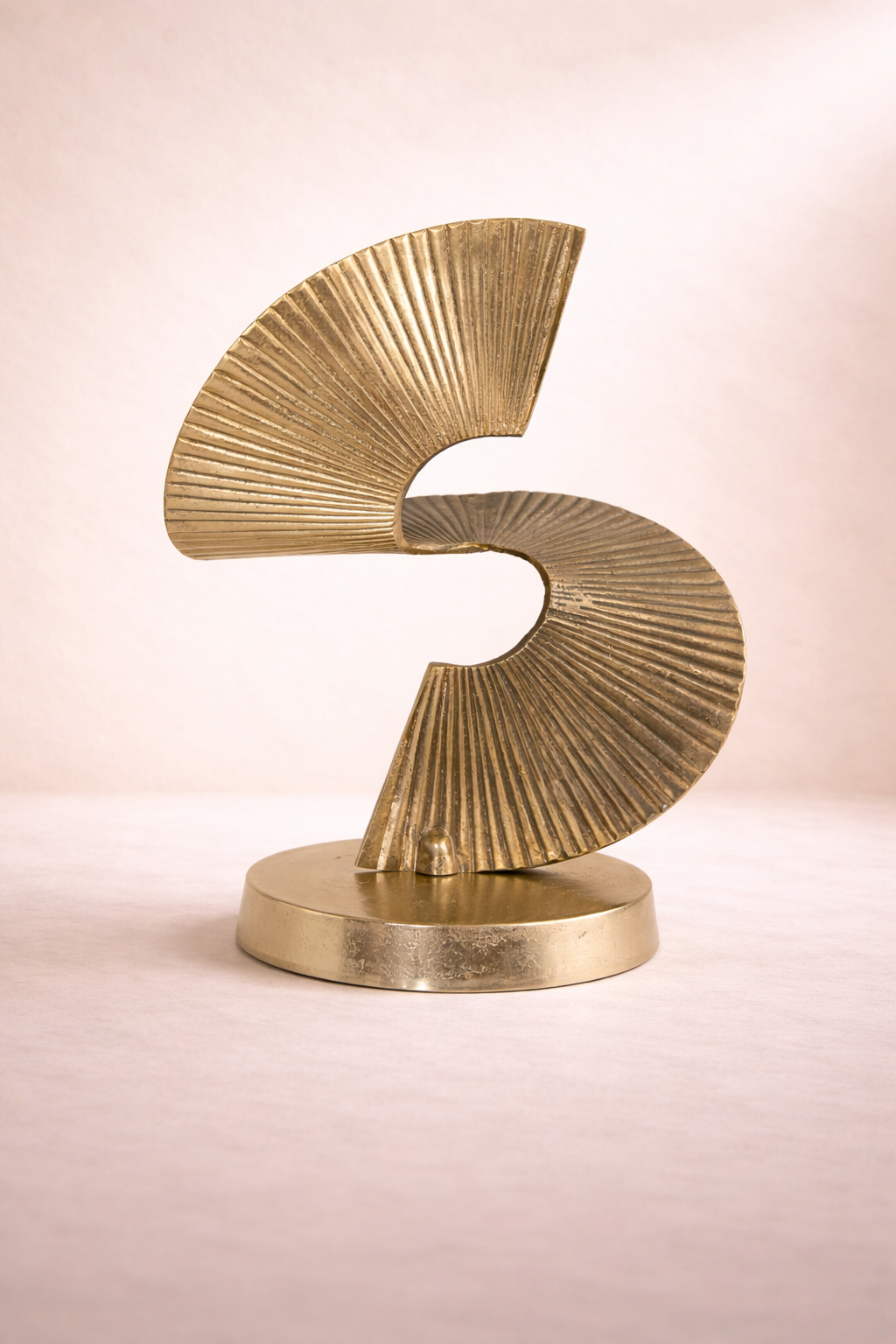 Gold abstract sculpture on a light pink background