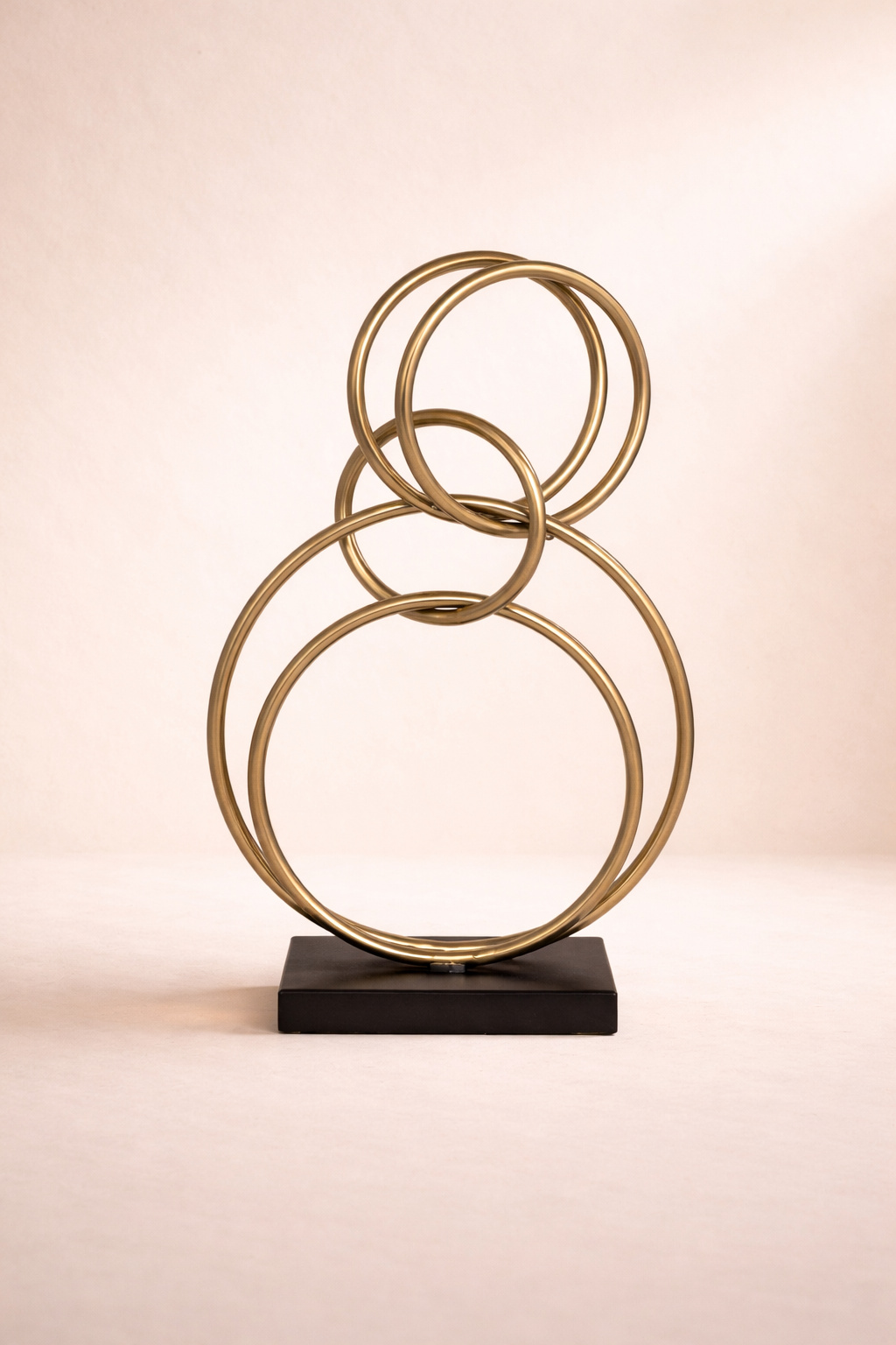 Decorative sculpture with interlocking gold rings on a black base against a beige background